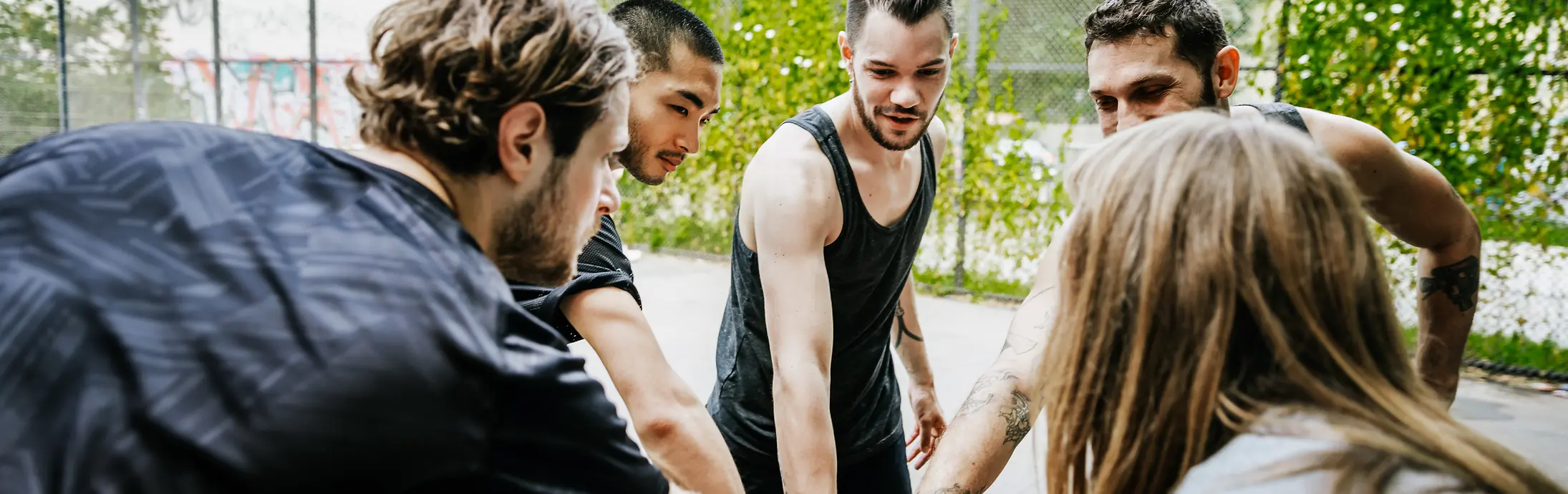 um grupo diversificado de jovens formando um círculo, cada um deles com uma mão no meio 