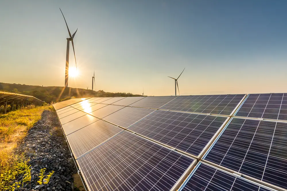 Painéis solares ao pôr do sol com moinhos de vento ao fundo