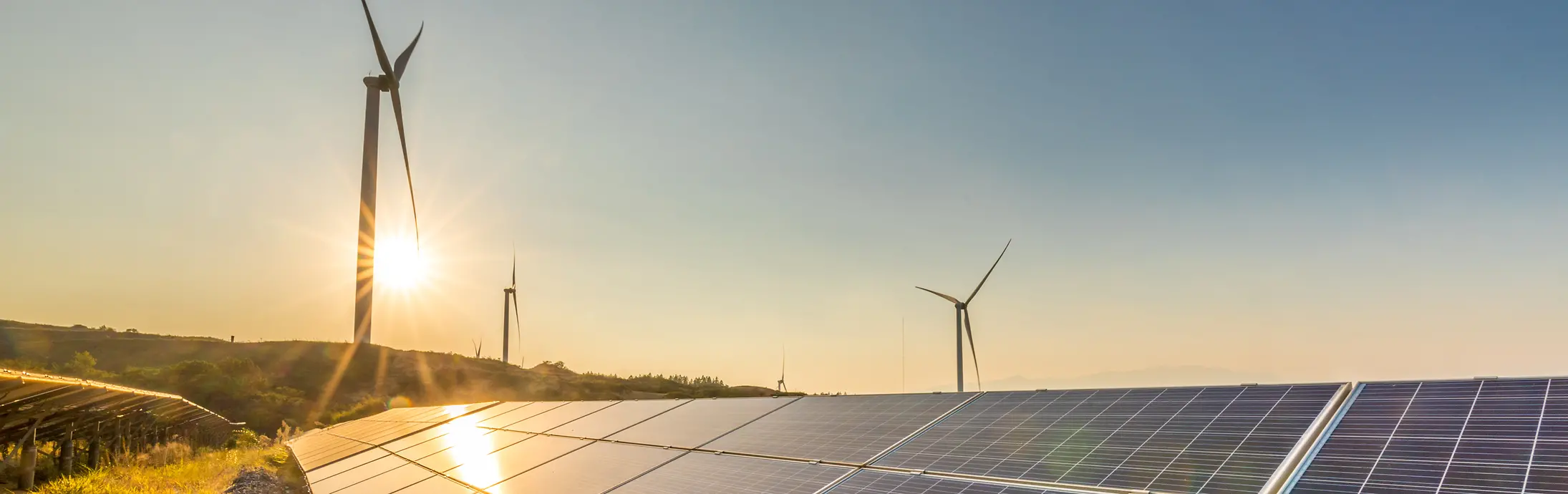 Painéis solares ao pôr do sol com moinhos de vento ao fundo