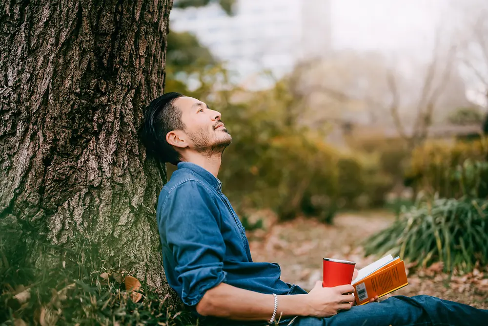 Um homem com um livro encostado em uma árvore