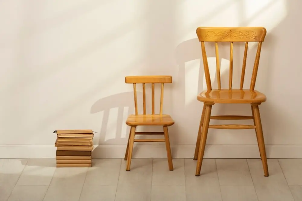 Imagem de duas cadeiras de madeiras e livros encostados em uma parede branca