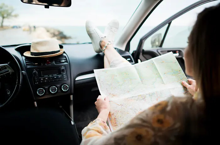 Uma passageira dentro do carro, segurando um mapa e prestes a viajar.